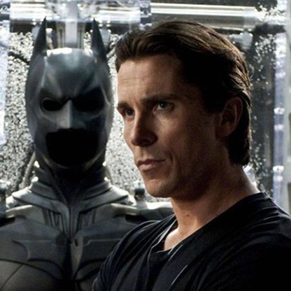Bruce Wayne karakteri Batman kostümünün yanında ciddiyetle dururken.