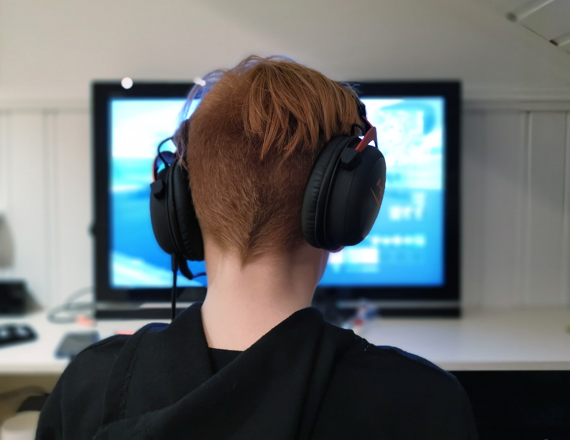 Bilgisayarın karşısında oyun oynayan kulaklıklı bir genç.
