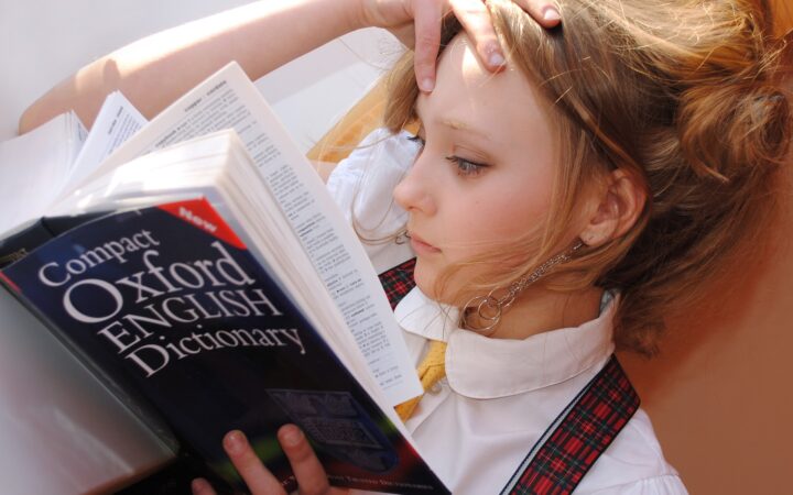 Bir öğrenci elini alnına koymuş, sözlük okuyor.