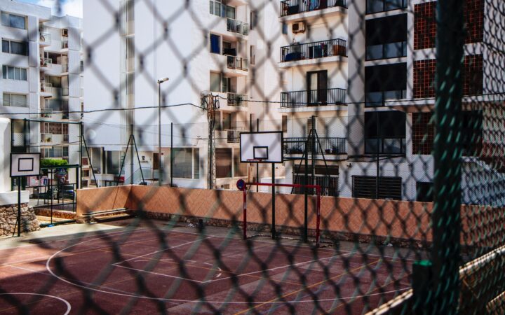 Boş bir basketbol-futbol sahası tel örgülerin ardından görünüyor.