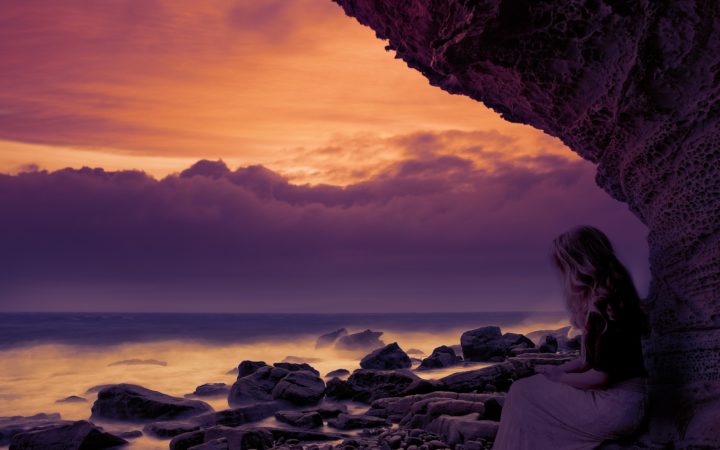 Gün batımında sahilde oturan beyazlı kadın.