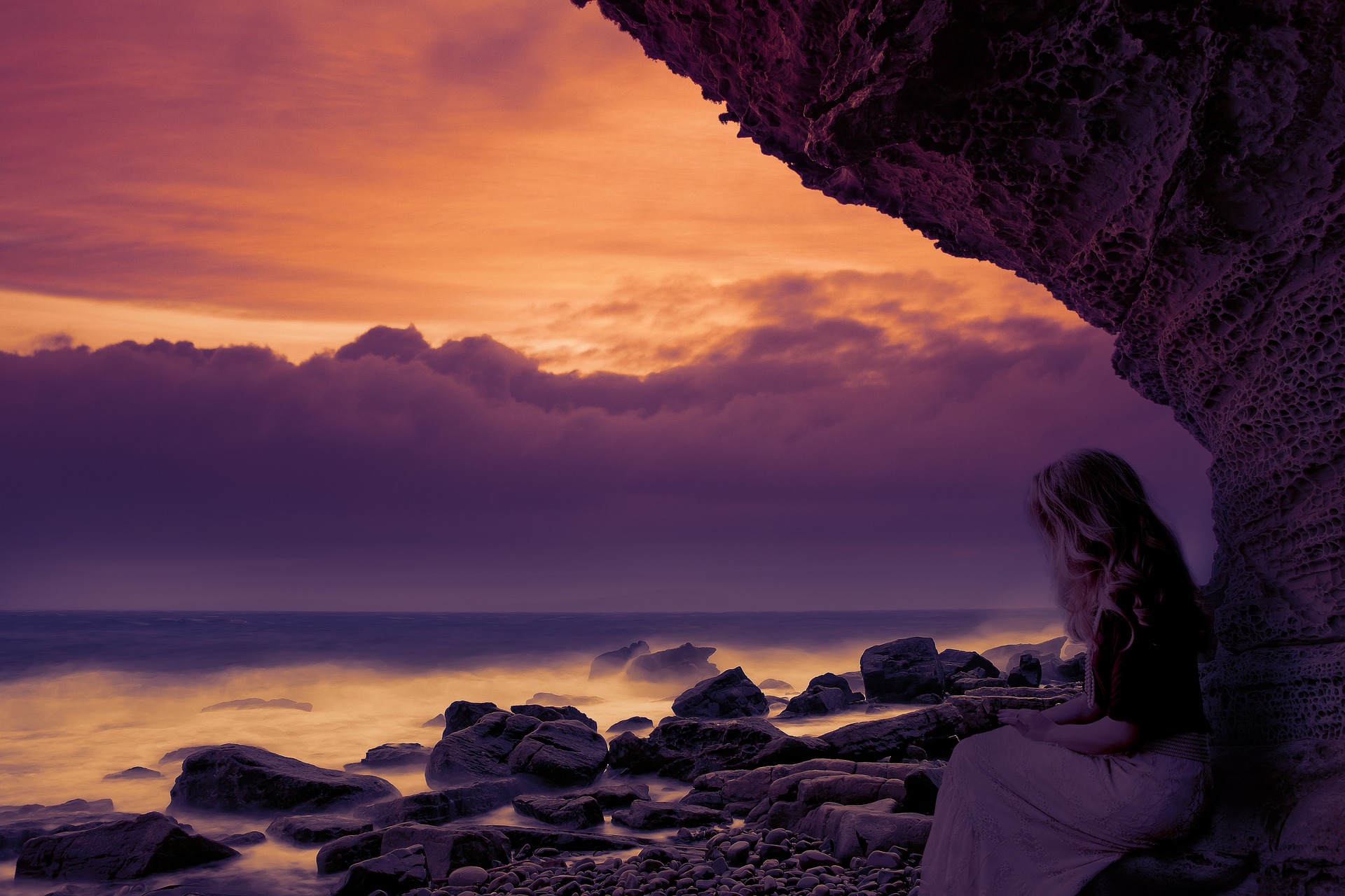 Gün batımında sahilde oturan beyazlı kadın.