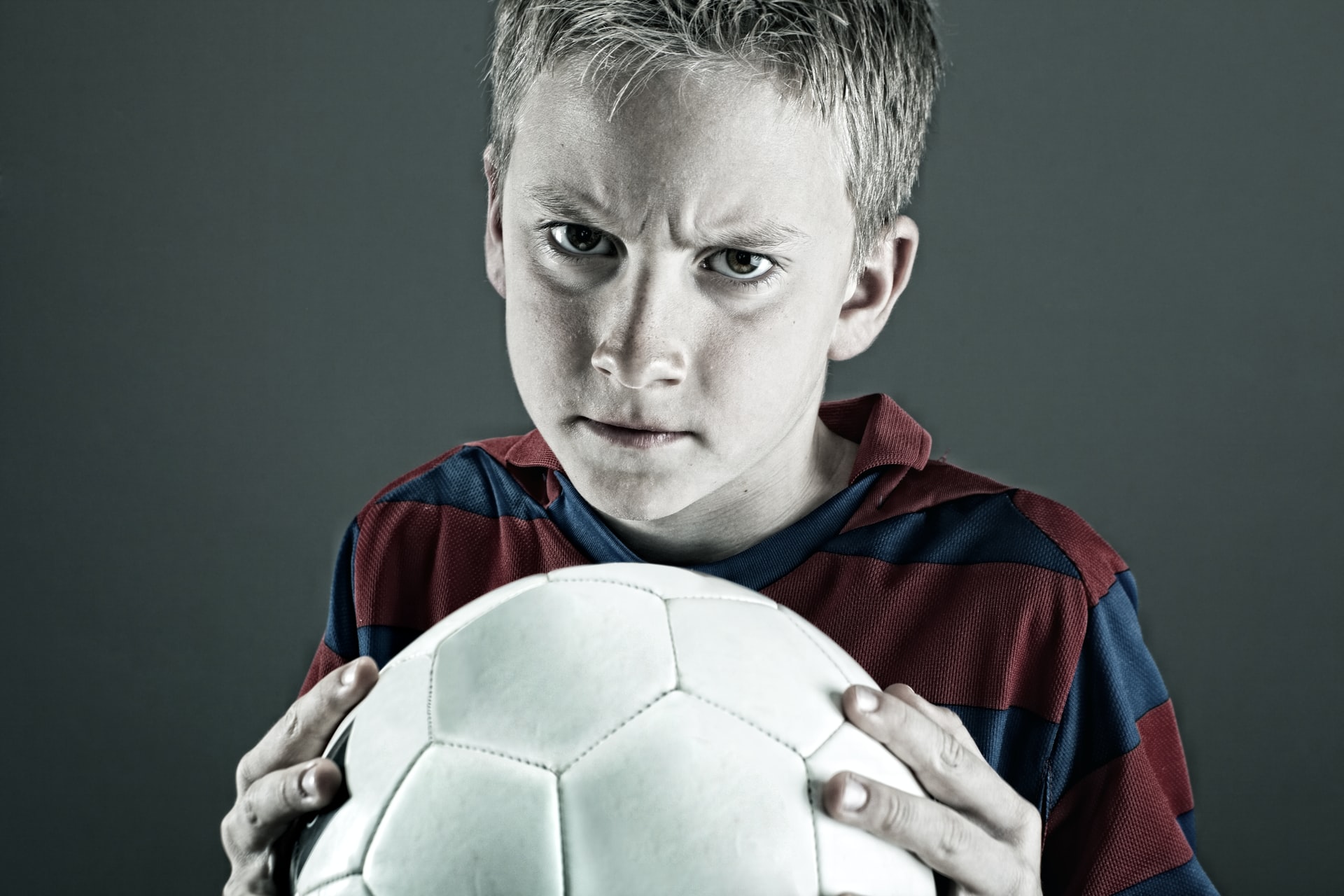 Futbol topunu sıkı sıkı tutan çocuk sinirli bakışlar atıyor.