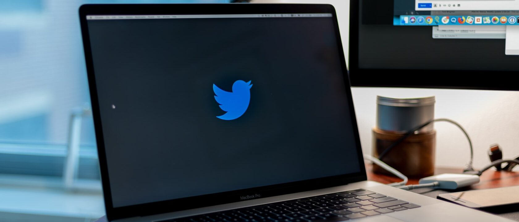 Masanın üzerinde duran bir laptop'un ekranında Twitter kuşu logosu var.