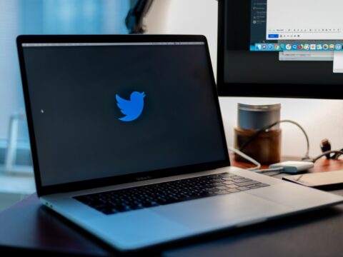 Masanın üzerinde duran bir laptop'un ekranında Twitter kuşu logosu var.