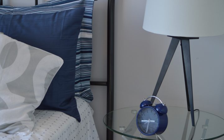 Yastıkların yanındaki cam sehpada duran mavi bir çalar saat.